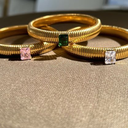 Three gold bangles with gemstones on a beige surface