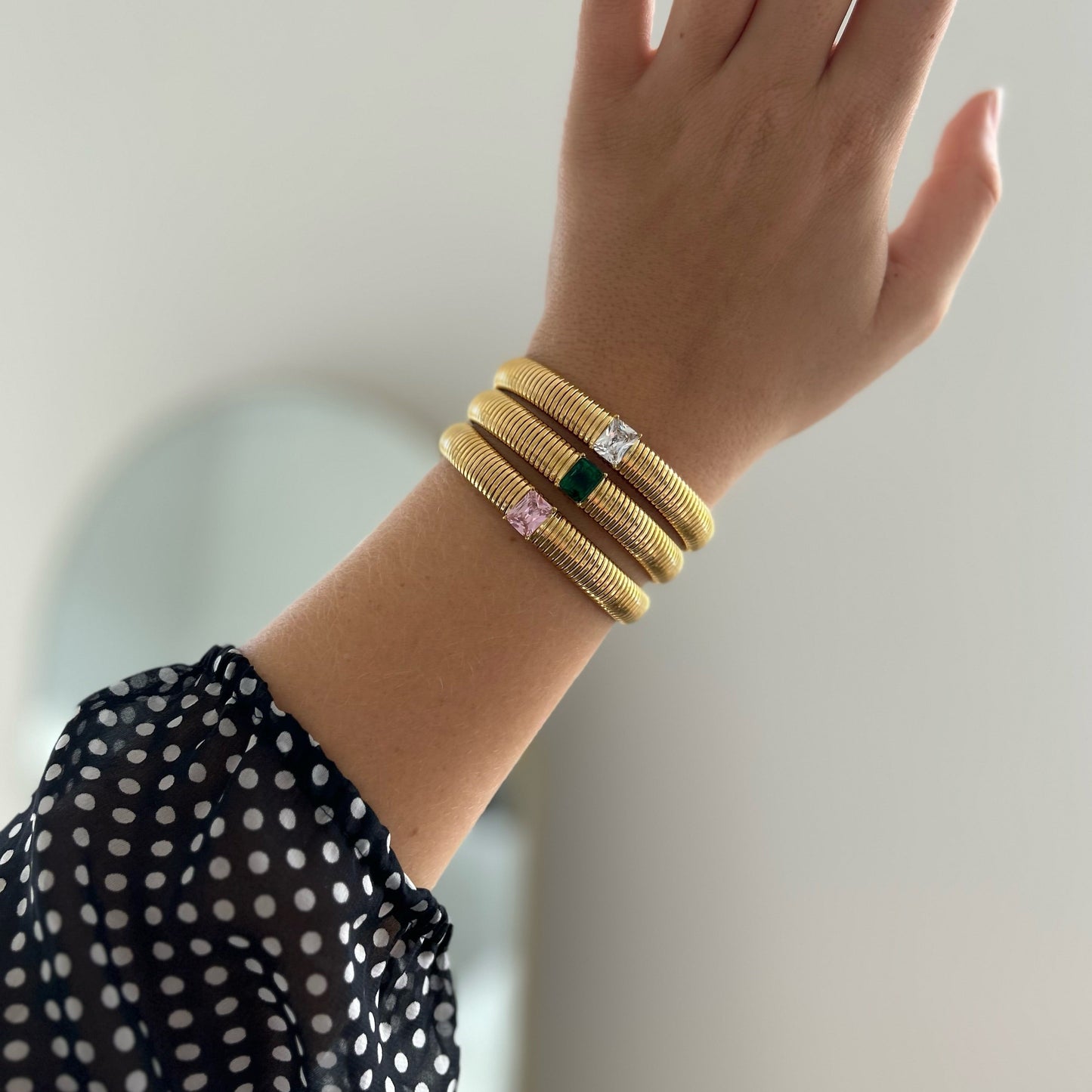 Hand wearing three yellow hair ties with decorative ends on a neutral background