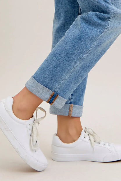 White sneakers and rolled-up blue jeans on a light background