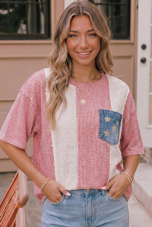 Woman wearing a red and white striped shirt with a denim pocket and blue jeans, standing in front of a beige building.