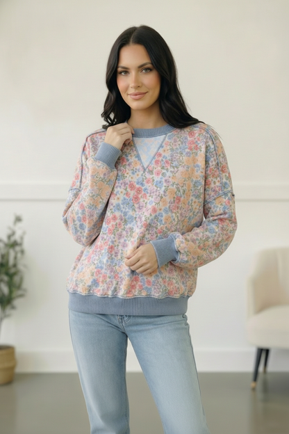 Woman wearing a floral sweater and light blue jeans indoors.