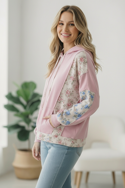 Woman wearing a pink floral hoodie in a bright room with a plant in the background