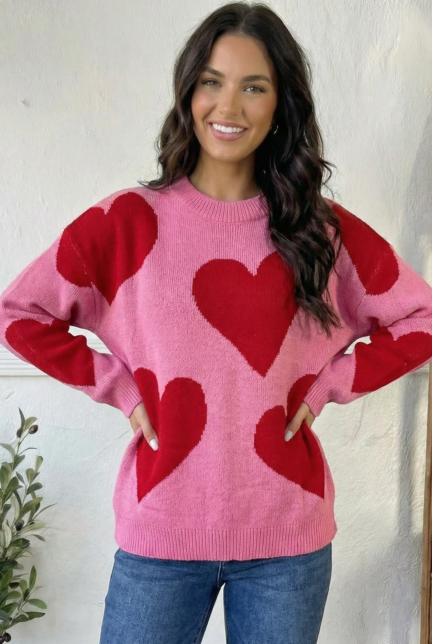 Woman wearing a pink sweater with red heart patterns against a white background