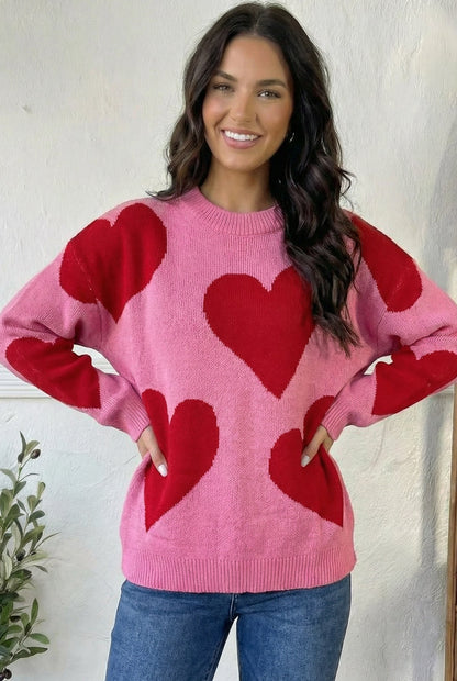 Woman wearing a pink sweater with red heart patterns against a white background