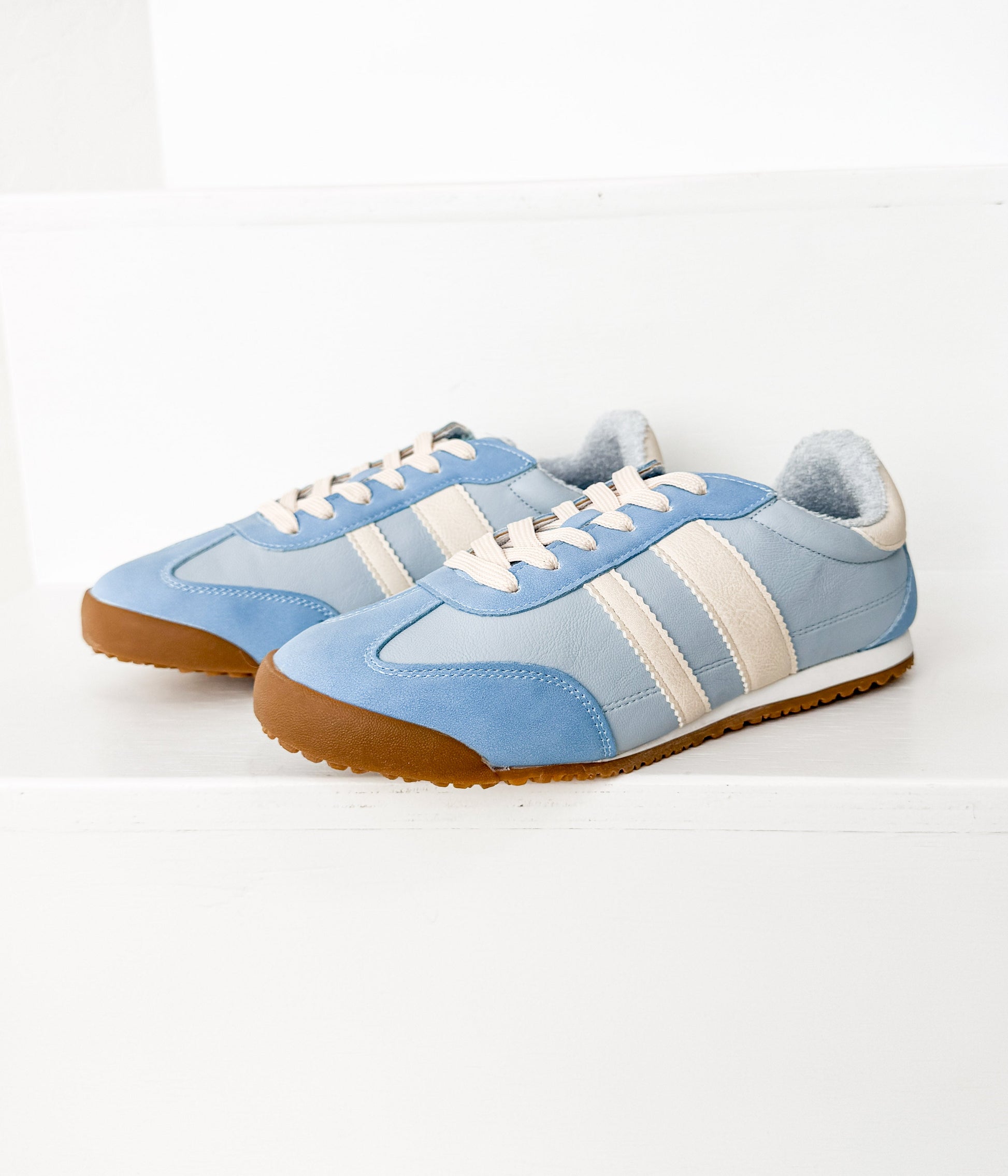 Pair of blue sneakers with white stripes on a light gray background