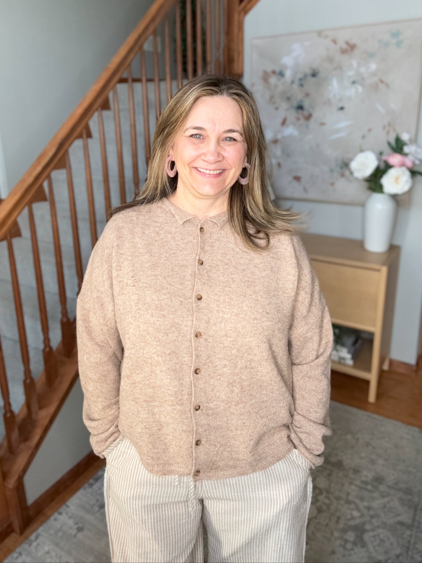 Woman standing in a home interior with wooden staircase and decor.