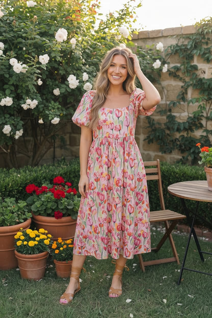 Woman in a floral dress standing in a garden with potted plants and flowers.