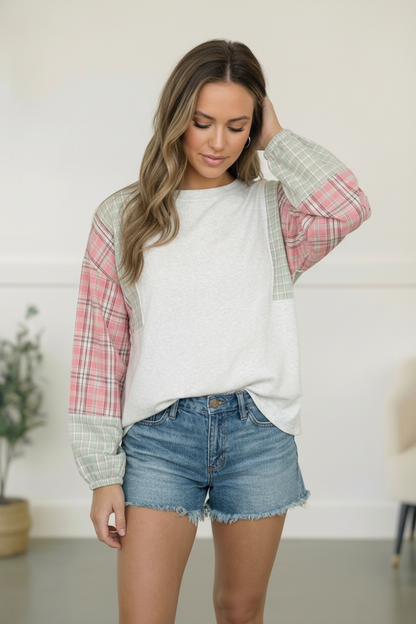 Woman wearing a plaid shirt over a white top with denim shorts indoors.