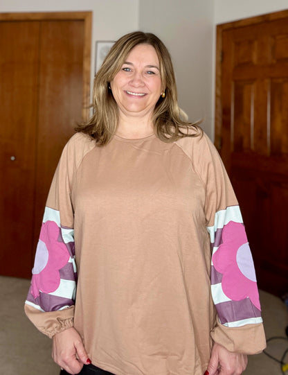 Woman wearing a beige long-sleeve top with floral patterns on the sleeves indoors.