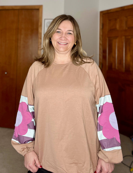 Woman wearing a beige long-sleeve top with floral patterns on the sleeves indoors.