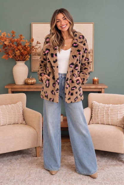 A woman stands in a living room wearing a beige leopard-print faux fur jacket over a white top and wide-leg light blue jeans.