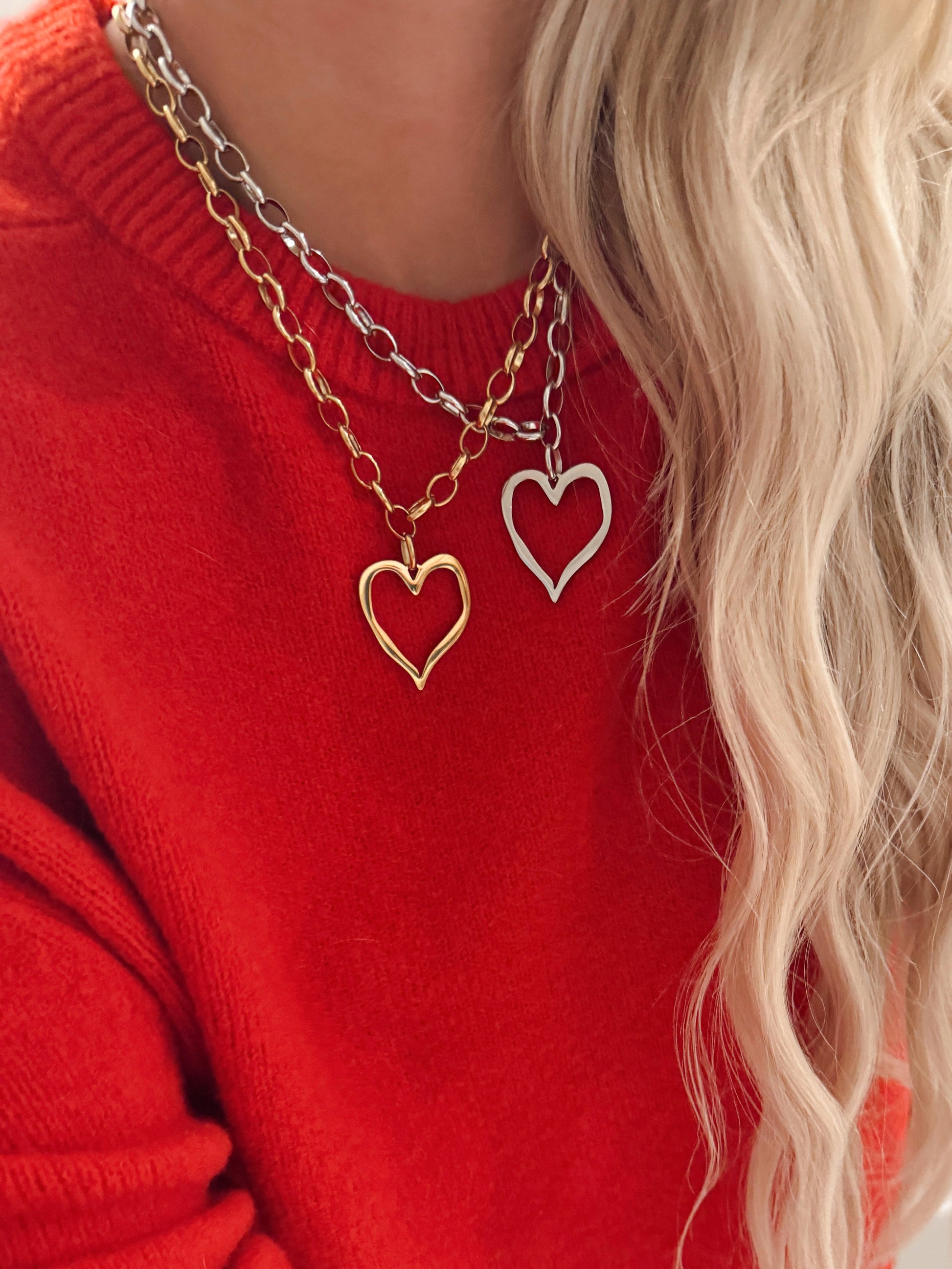 Person wearing a red sweater with layered heart-shaped necklaces.