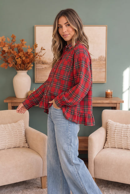 A woman modeling a red and black plaid flannel shirt with a ruffled hem, paired with light blue jeans, standing in a cozy living room setting.