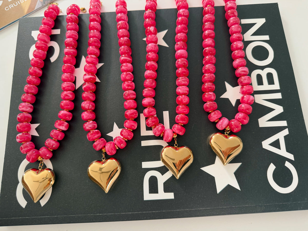 Four pink beaded hair ties with gold heart charms, arranged on a black display card with white stars and the brand name 'CAMBON'.