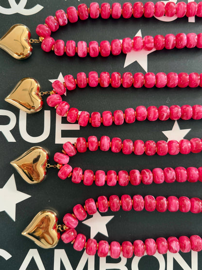 Pink marbled bead strands with gold heart charms, arranged on a dark background with white star and letter graphics.