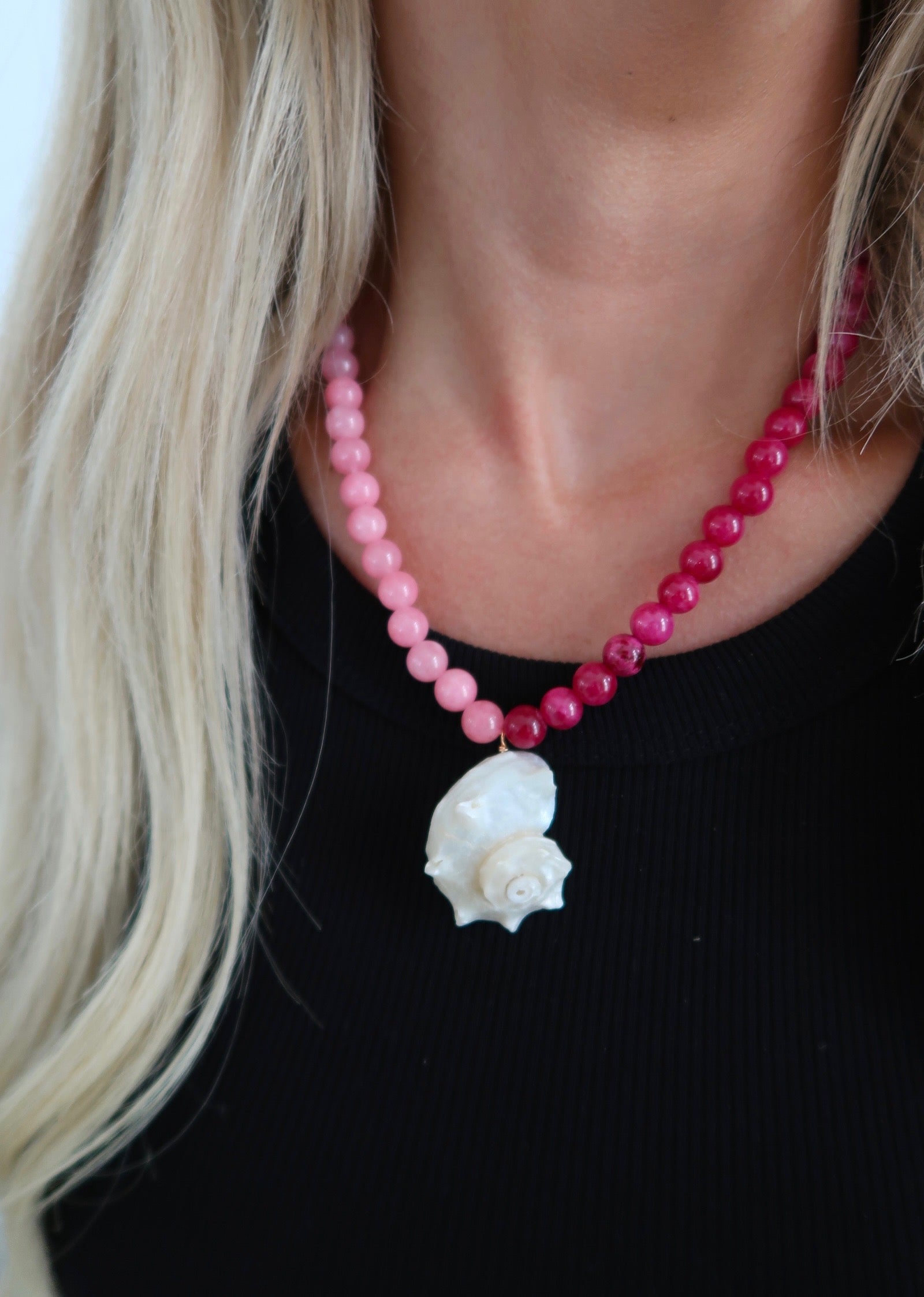 Necklace with pink beads and a white flower pendant worn by a person with blonde hair.