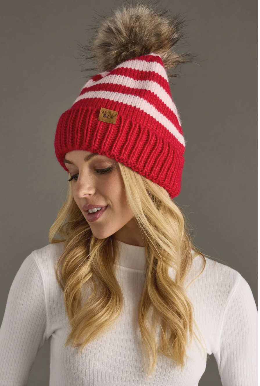 Woman wearing a red and white striped beanie with a fur pom-pom on a gray background