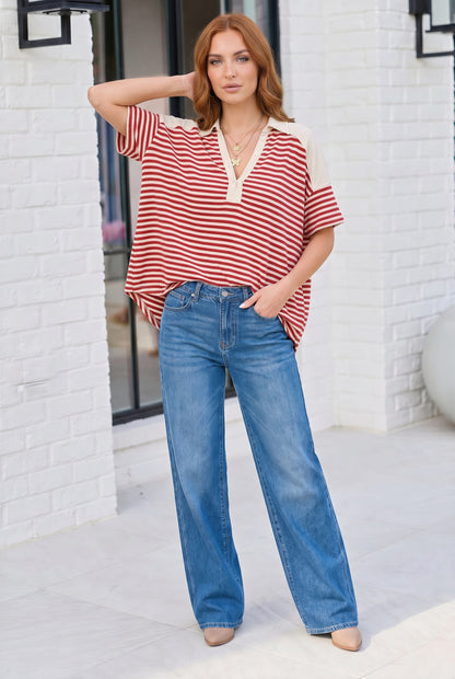 Woman wearing a red and white striped shirt and blue jeans standing against a white brick wall.
