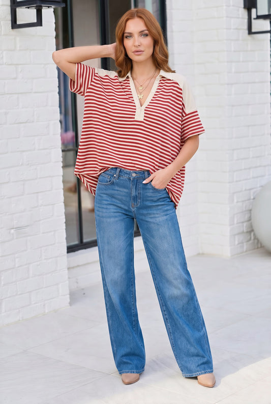 Woman wearing a red and white striped shirt and blue jeans standing against a white brick wall.