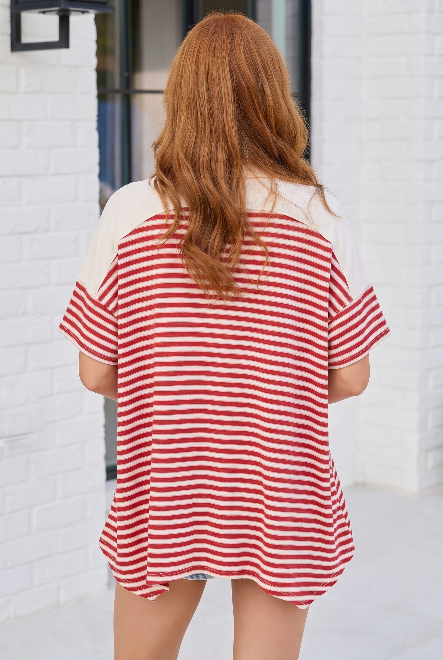 Person wearing a red and white striped shirt in front of a white brick wall.