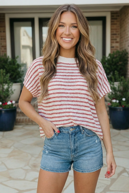 Woman wearing a red and white striped shirt and blue shorts standing outdoors.