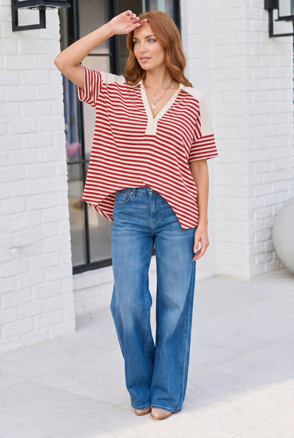 Woman wearing a red and white striped shirt and blue jeans standing against a white brick wall.