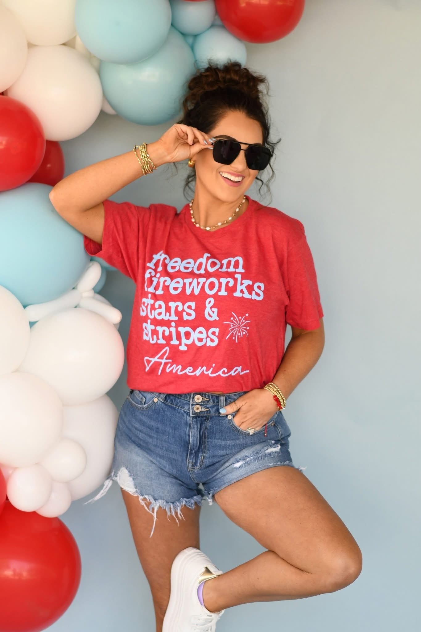 Woman wearing a red t-shirt with patriotic text, standing in front of balloons.
