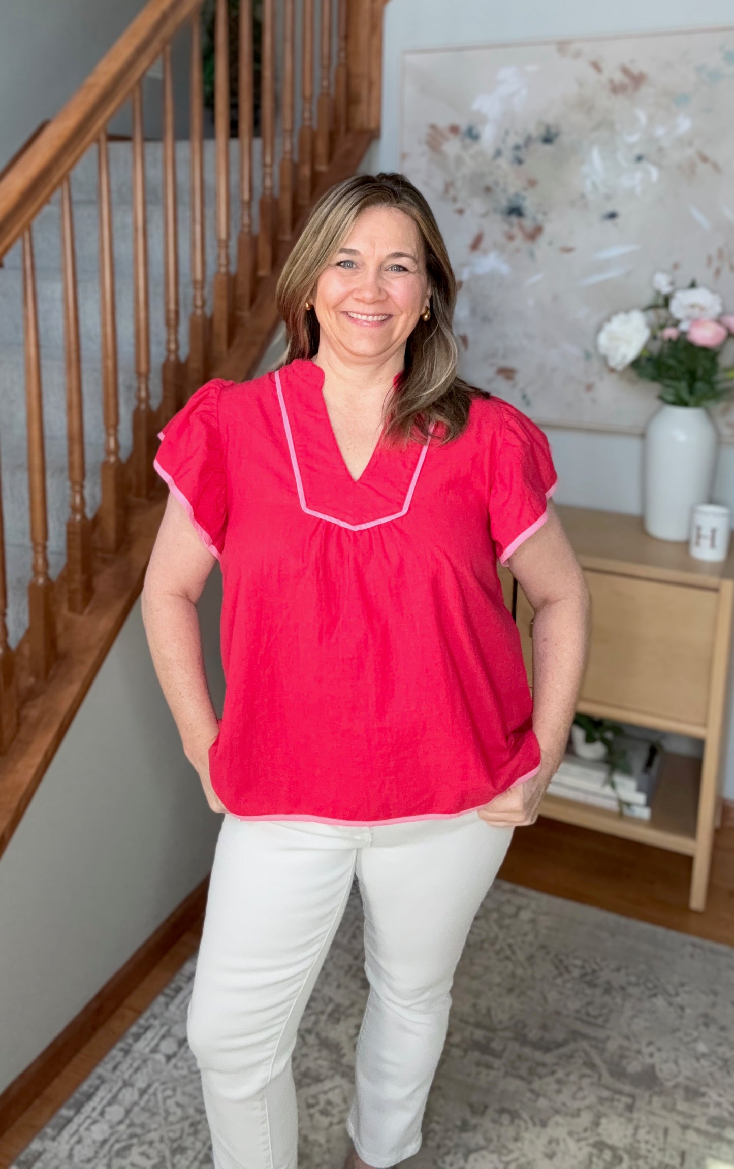Woman wearing a red blouse with white trim standing in a home setting.
