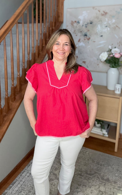 Woman wearing a red blouse with white trim standing in a home setting.