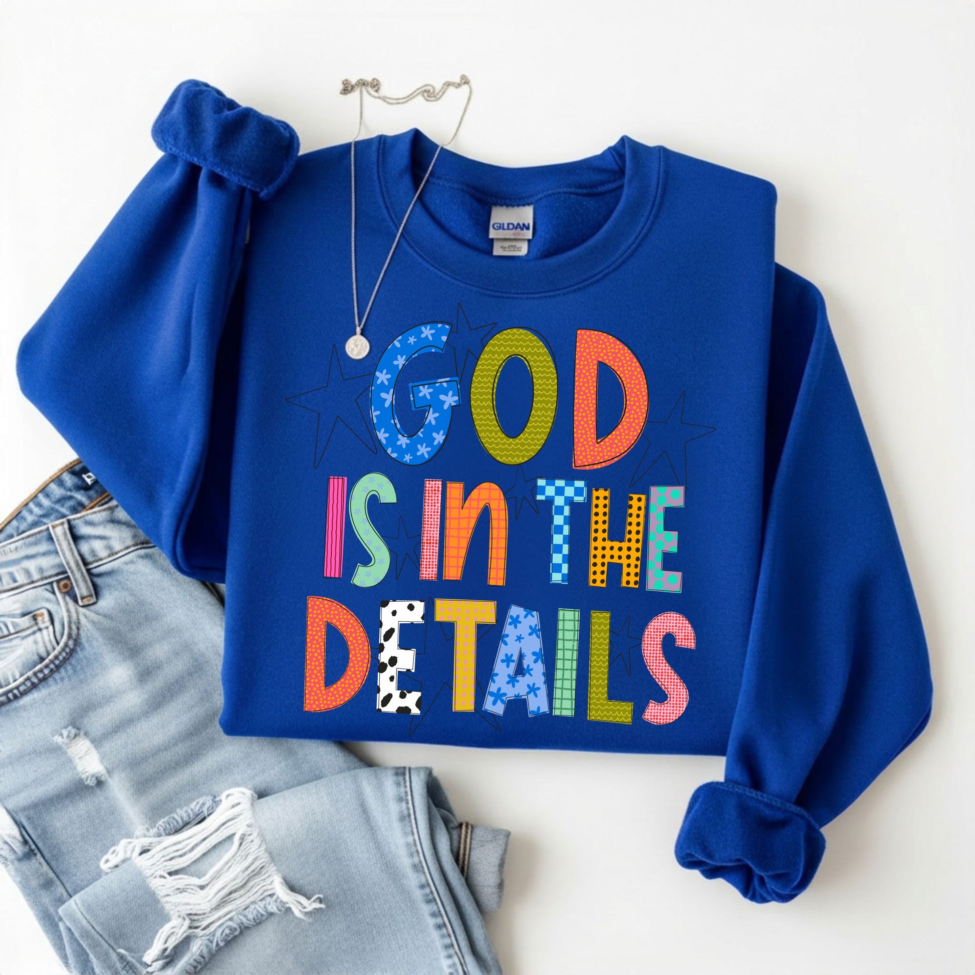 Blue sweatshirt with colorful text 'GOD IS IN THE DETAILS' on a white background