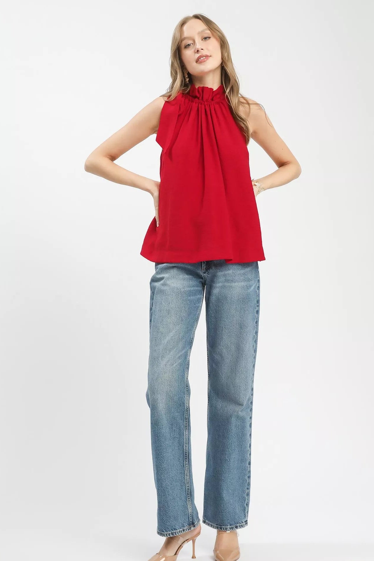 Woman wearing a red sleeveless top and blue jeans on a white background