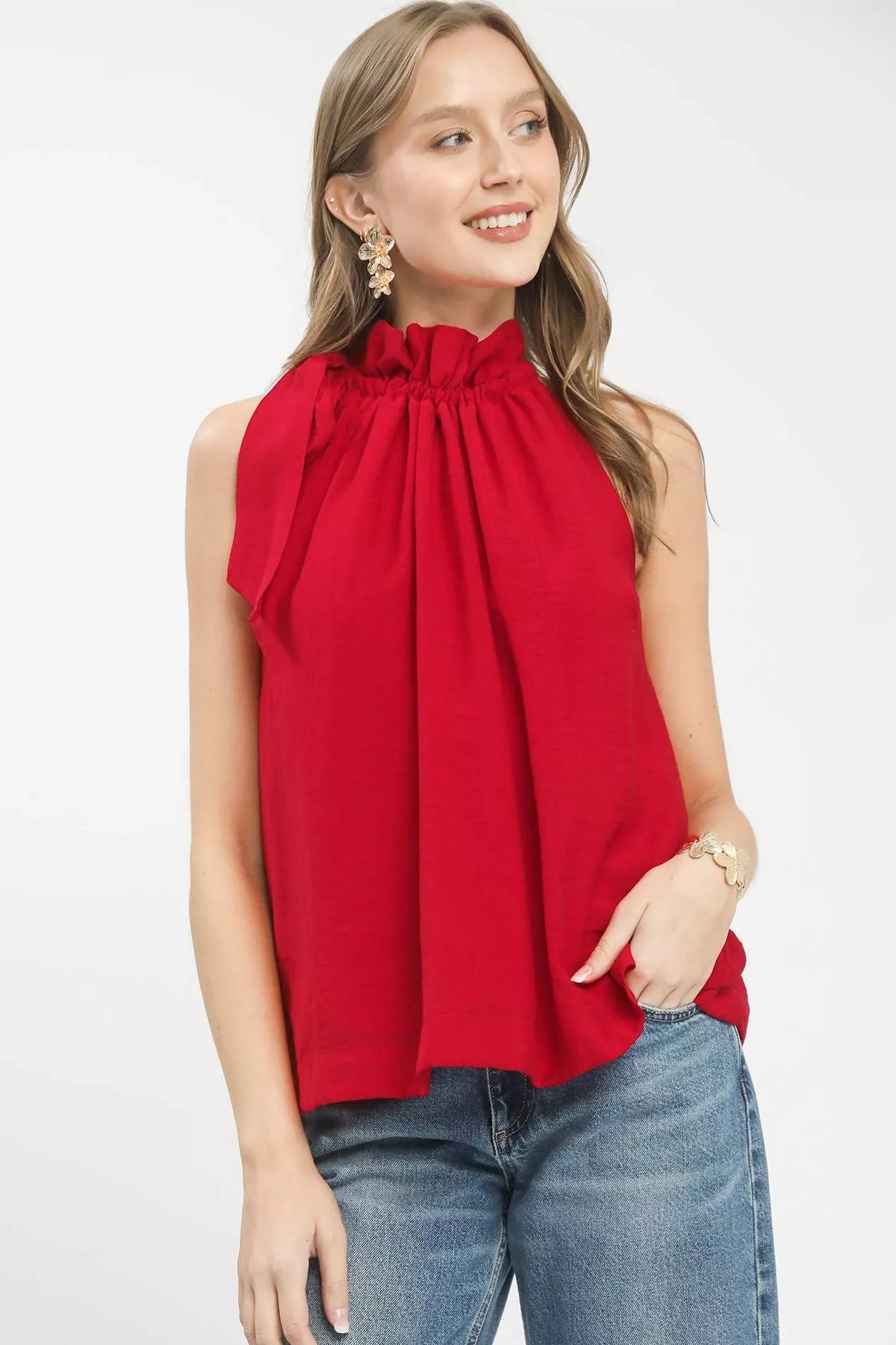 Woman wearing a red sleeveless top with a bow detail and blue jeans on a white background