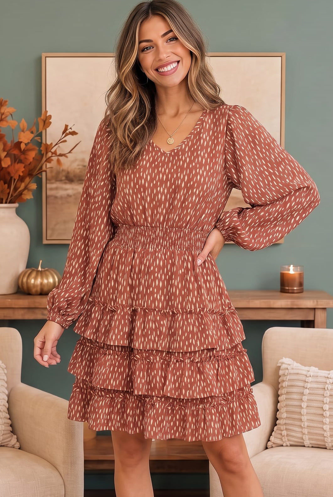 A woman wearing a rust-brown and cream patterned tiered mini dress with long puff sleeves, standing in a cozy living room setting.