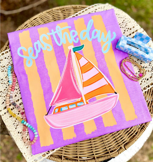 Sailboat design on a purple towel with 'Seas the day' text, placed on a woven surface.