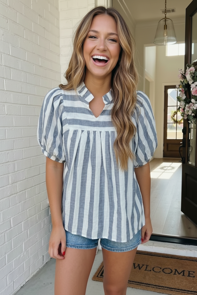 Woman wearing a blue and white striped shirt and denim shorts, standing indoors.