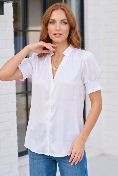 Woman wearing a white blouse and blue jeans standing against a white brick wall.