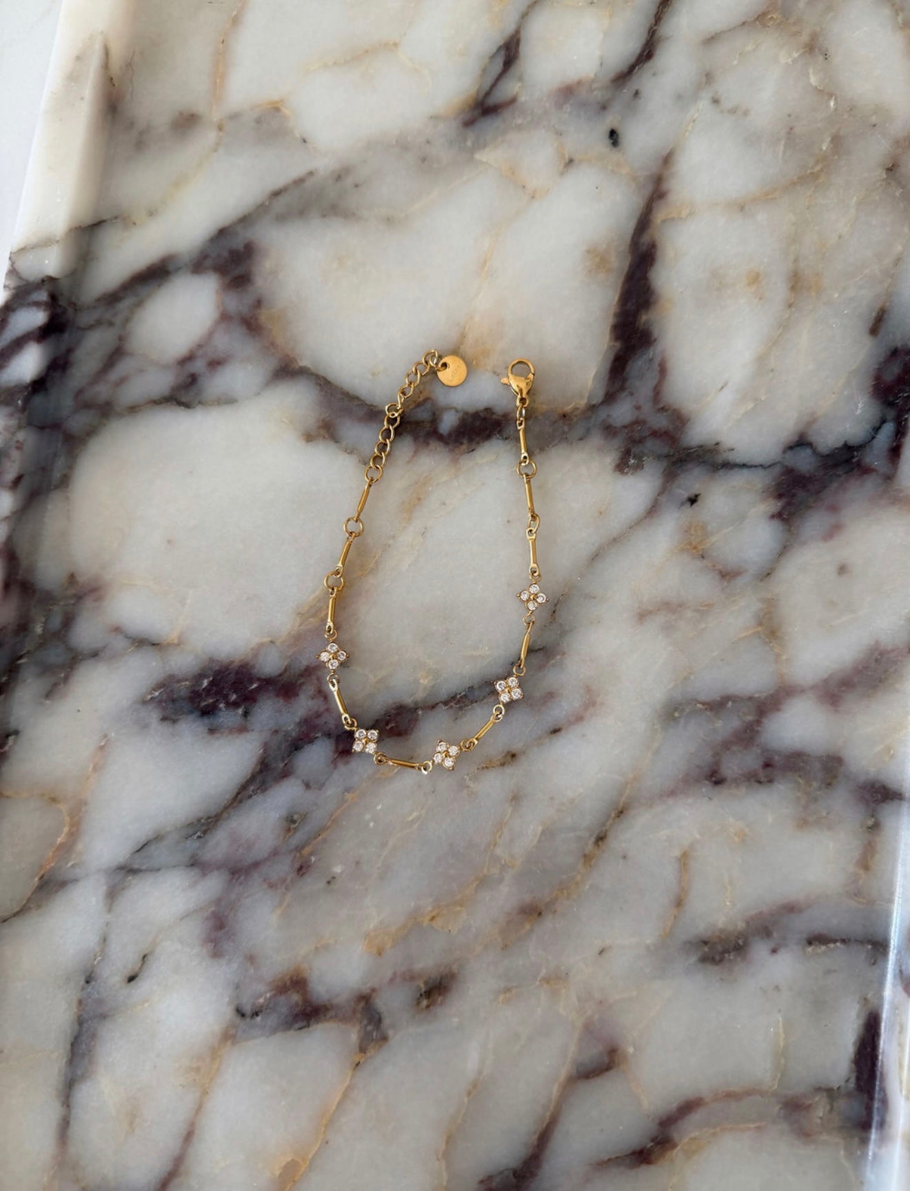 A delicate gold chain bracelet with small floral star details and a gold clasp, displayed on a white and gray veined marble surface.