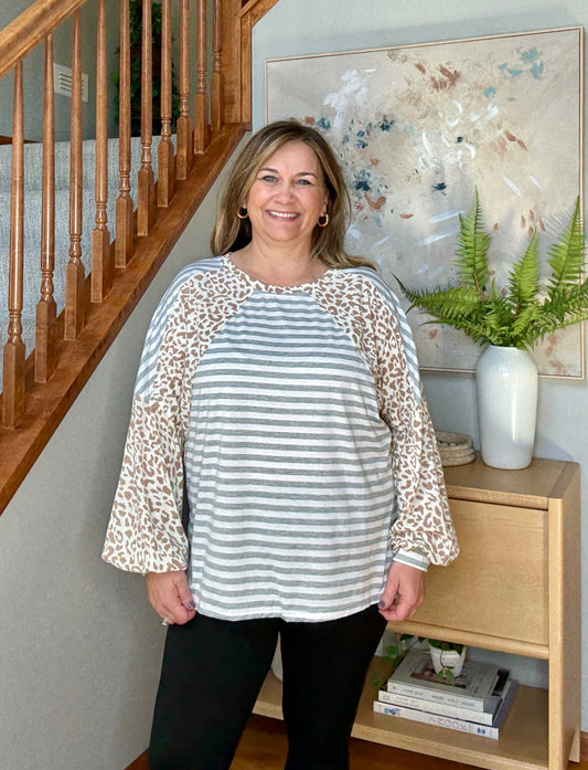 Woman wearing a striped shirt with leopard print sleeves standing in a home setting.