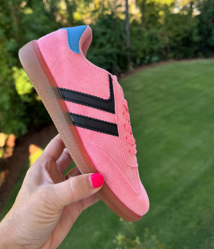 Pink sneaker with black stripes held by a hand against a blurred green outdoor background