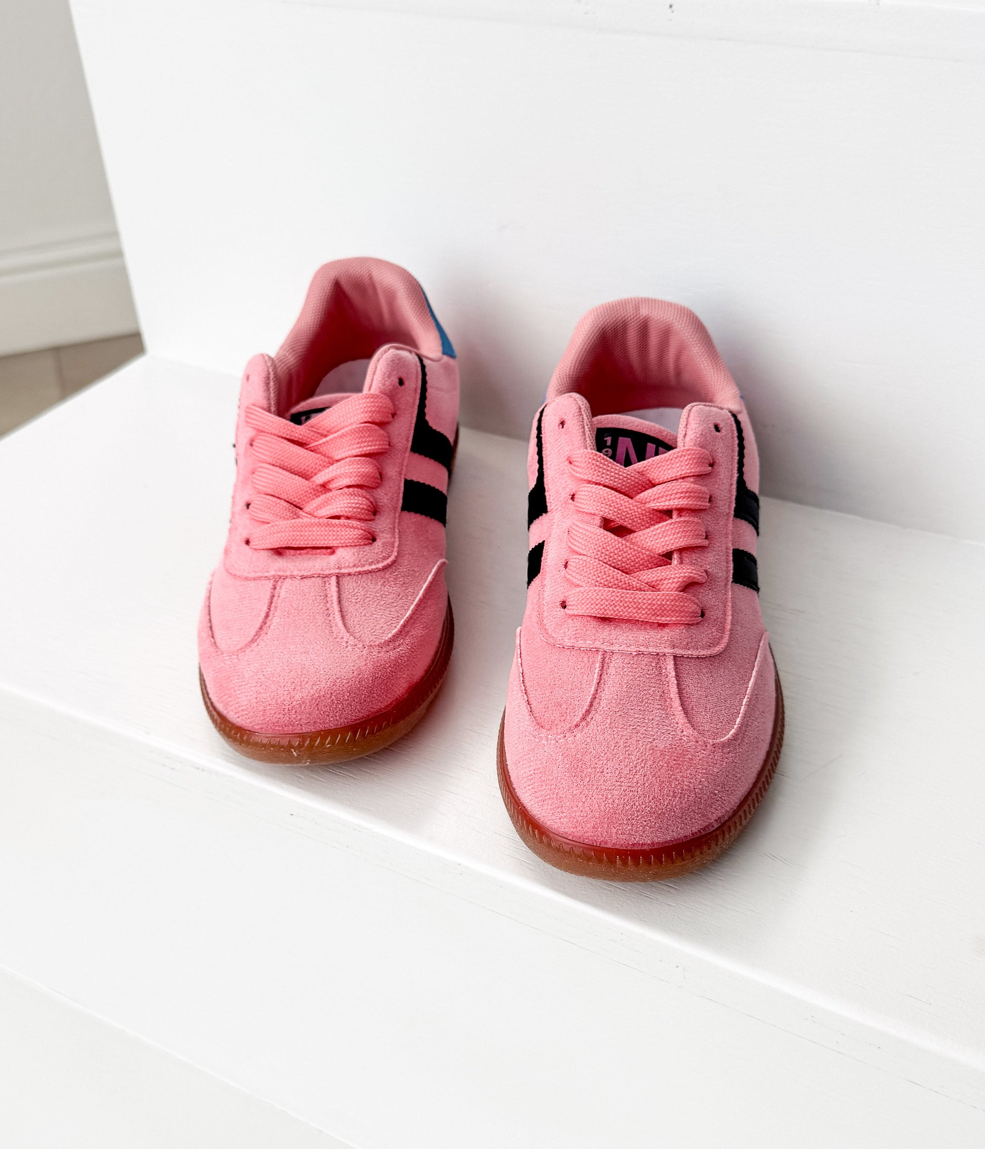 Pair of pink sneakers with black stripes on a white surface