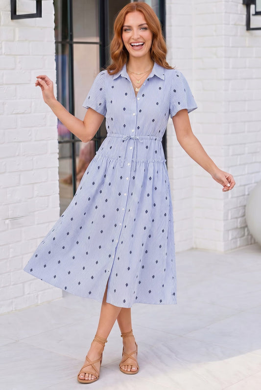 Woman wearing a light blue polka dot dress standing against a white brick wall.