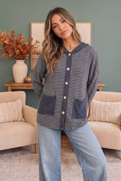 A woman modeling a navy and gray striped hooded cardigan with corduroy pockets in a cozy living room setting.