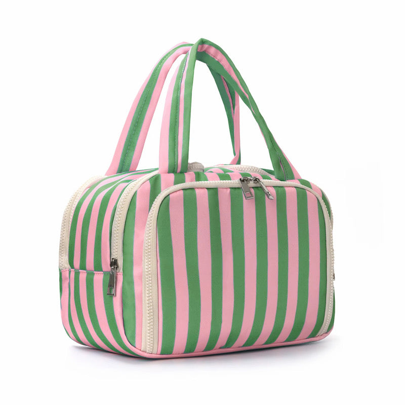 A striped soft-sided bag with vertical pink and green stripes, cream-colored zippers, and dual top handles, shown on a plain white background.