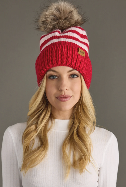 Woman wearing a red and white striped beanie with a fur pom-pom on a gray background