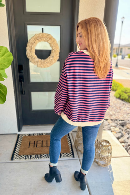 women in front of a front door of home in jeans, black booties, and a striped long sleeve pink, navy, and yellow pullvoer