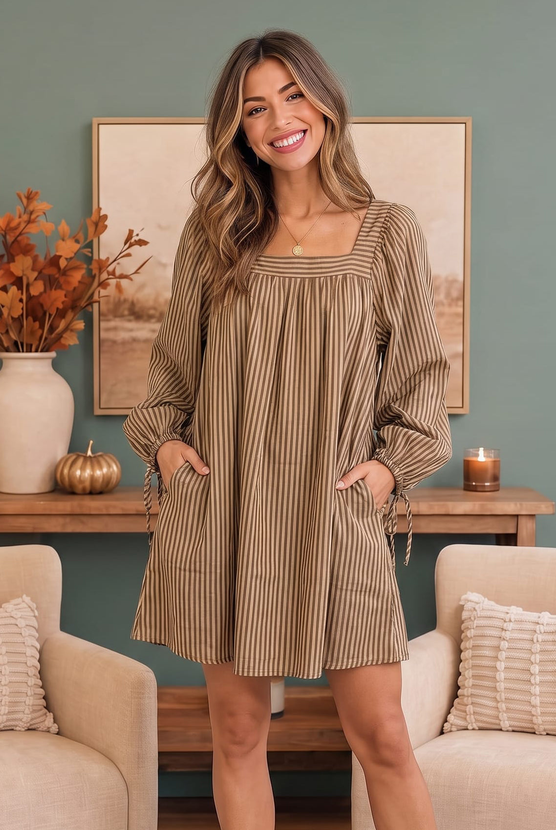 A woman modeling a brown and beige vertically striped mini dress with a square neckline, long sleeves, and side pockets in a cozy living room setting.