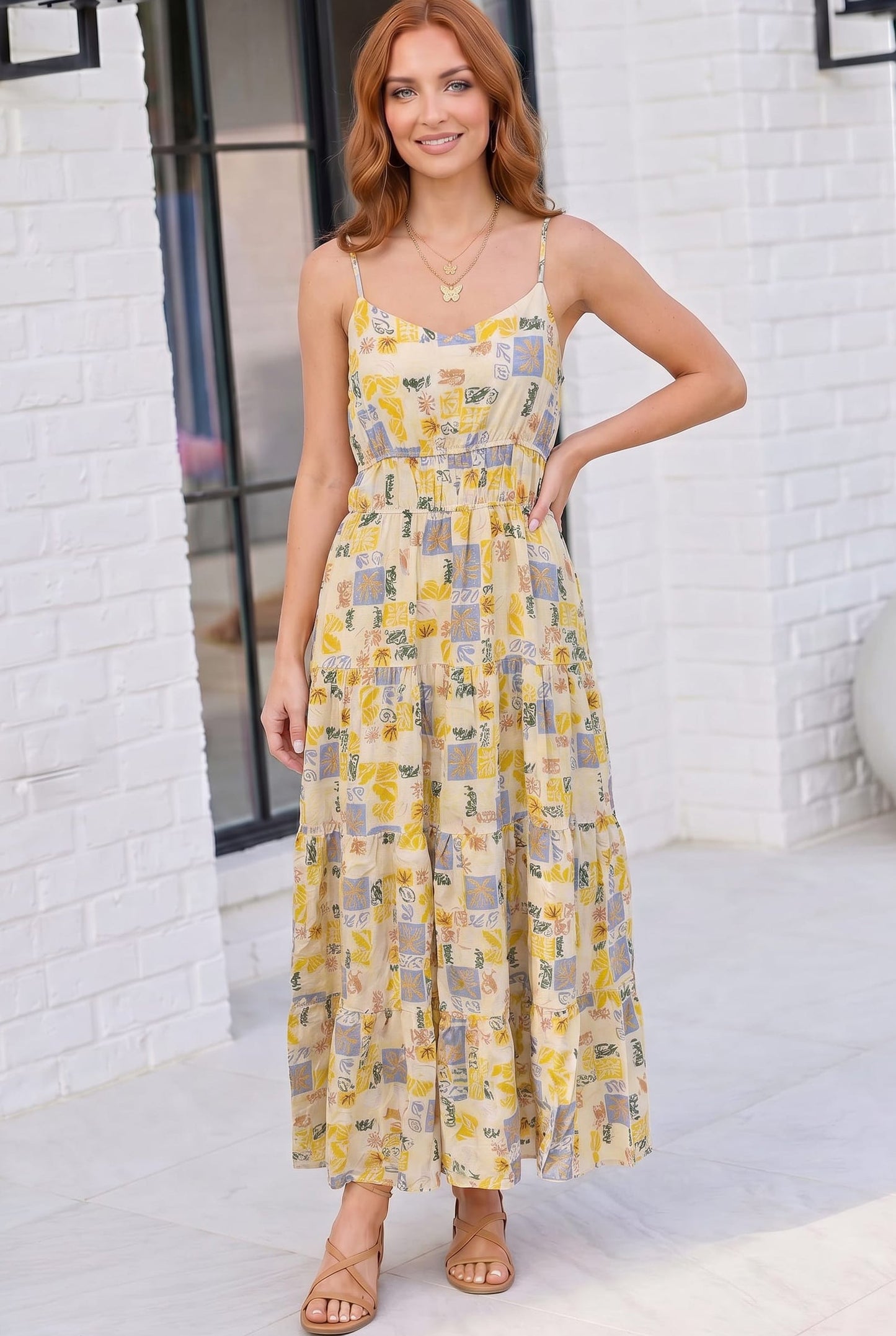 Woman wearing a yellow floral dress against a white brick wall.