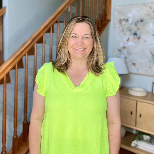 Woman in a bright green shirt standing in a home interior with a staircase and decor.