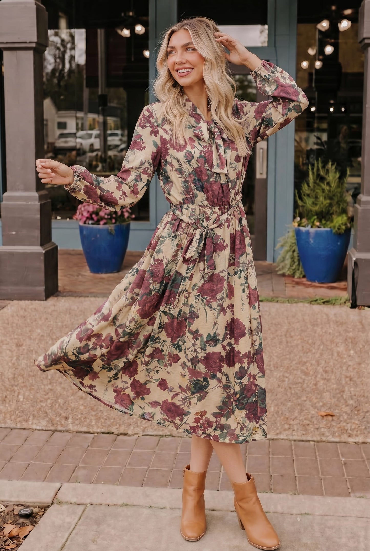 Woman wearing a floral dress standing outdoors with plants and a building in the background