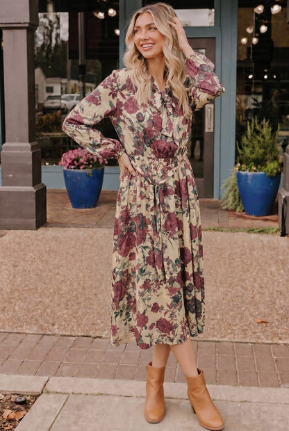 Woman wearing a floral dress standing outdoors with plants and a building in the background
